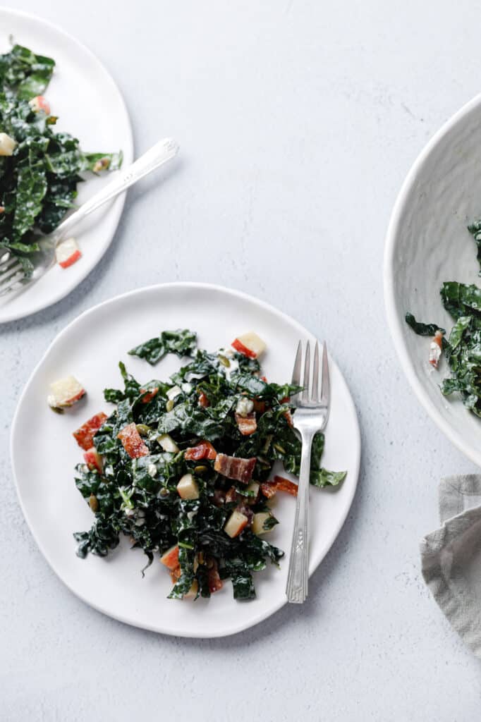 a plate of kale salad with bacon and apples in a creamy dressing