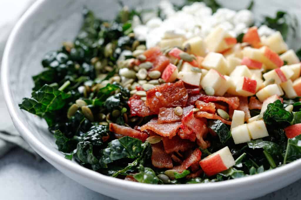 A close up of a bowl of kale salad with crispy bacon.