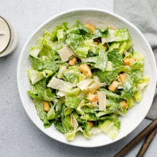 overhead view of a bowl of Caesar salad with tongs and dressing on the side