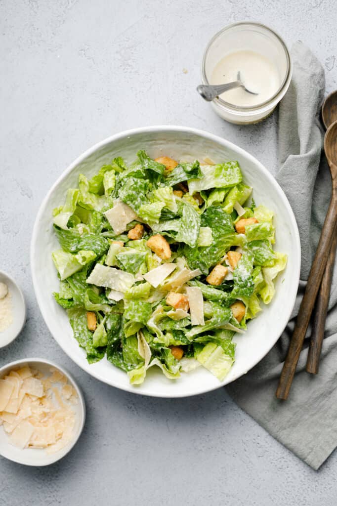 Overhead view of assembled Caesar Salad with tongs and two types of parmesan cheese