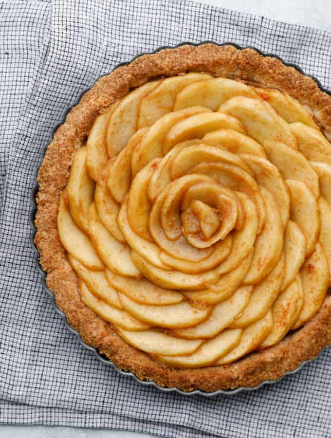 Overhead view of an apple tart with spiraled apples, with a knife to the side and plates with forks ready to serve the pie