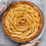 Overhead view of an apple tart with spiraled apples fresh out of the oven being held with two hands an a kitchen towel