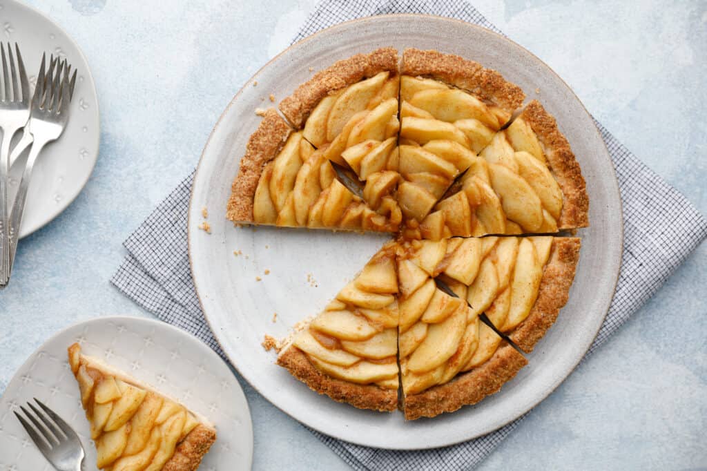 An overhead view of an apple tart with a slice removed and on a plate beside the full tart