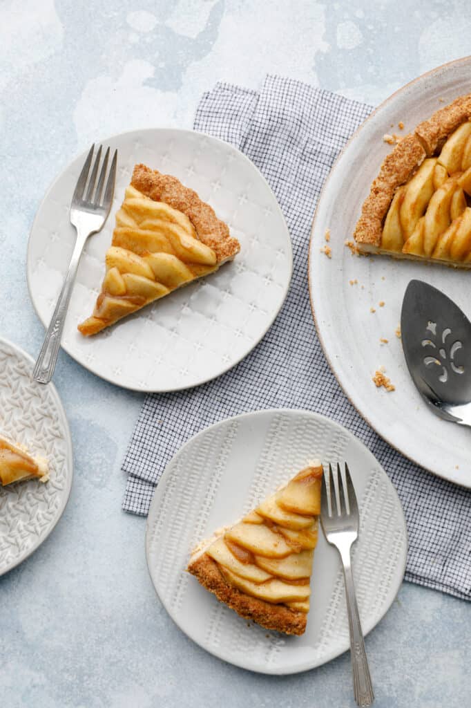 Slices of Vegan Apple Tart with homemade apple butter on white plates with a blue background ready to be eaten
