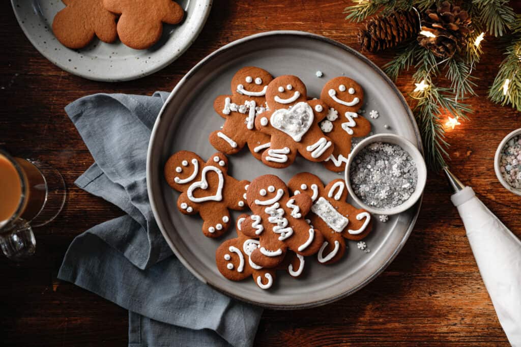 Overhead image of a plate of gingerbread cookies with holiday lights, sprinkles and a piping bag