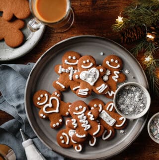 Overhead image of a plate of gingerbread cookies with holiday lights, sprinkles and a piping bag