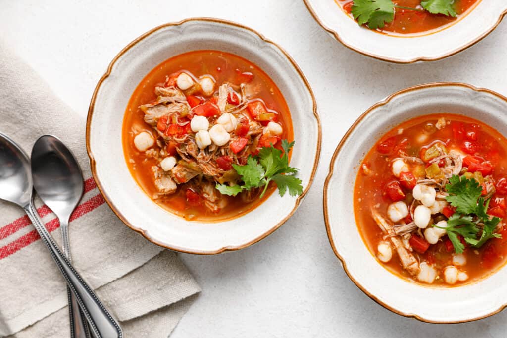 overhead image of bowls of red posole with pork and hominy