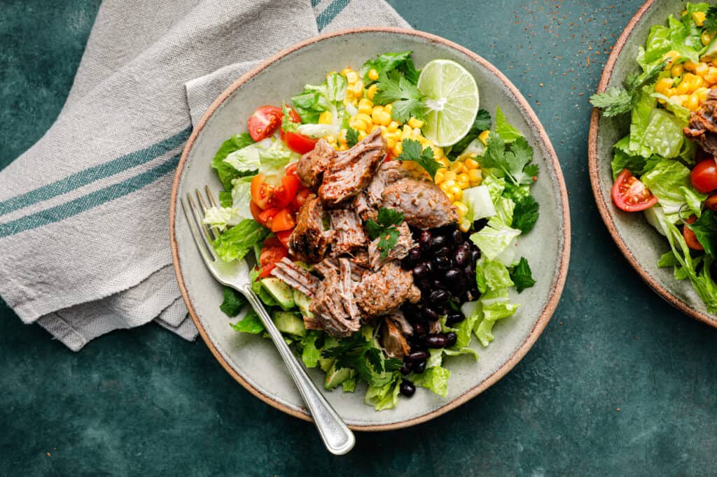 vista aérea de una ensalada con carne de cerdo rallada, lechuga, tomates, aguacate y frijoles negros