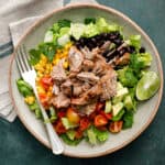 overhead view of a salad with shredded pork, lettuce, tomatoes, avocado and black beans