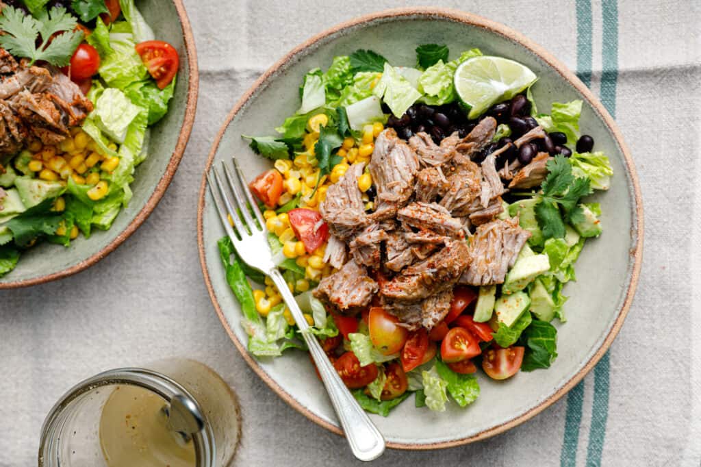overhead view of a salad with shredded pork, lettuce, tomatoes, avocado and black beans