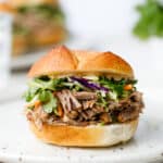 Head on shot of a pulled pork sandwich with broccoli slaw on a white plate