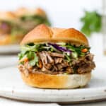 Head on shot of a pulled pork sandwich with broccoli slaw on a white plate