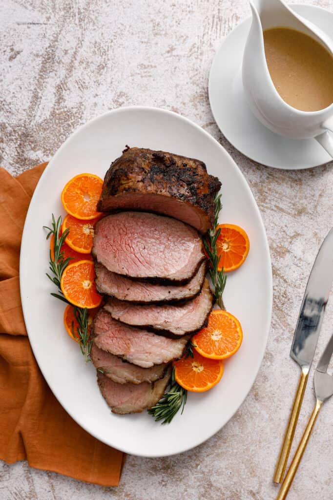 Overhead view of a slice beef roast on a platter with citrus and rosemary.