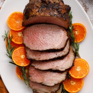 overhead view of a beef roast, sliced and surrounded by citrus and rosemary