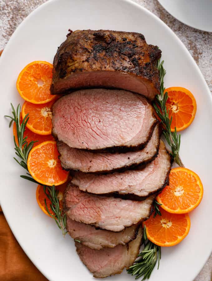 overhead view of a beef roast, sliced and surrounded by citrus and rosemary
