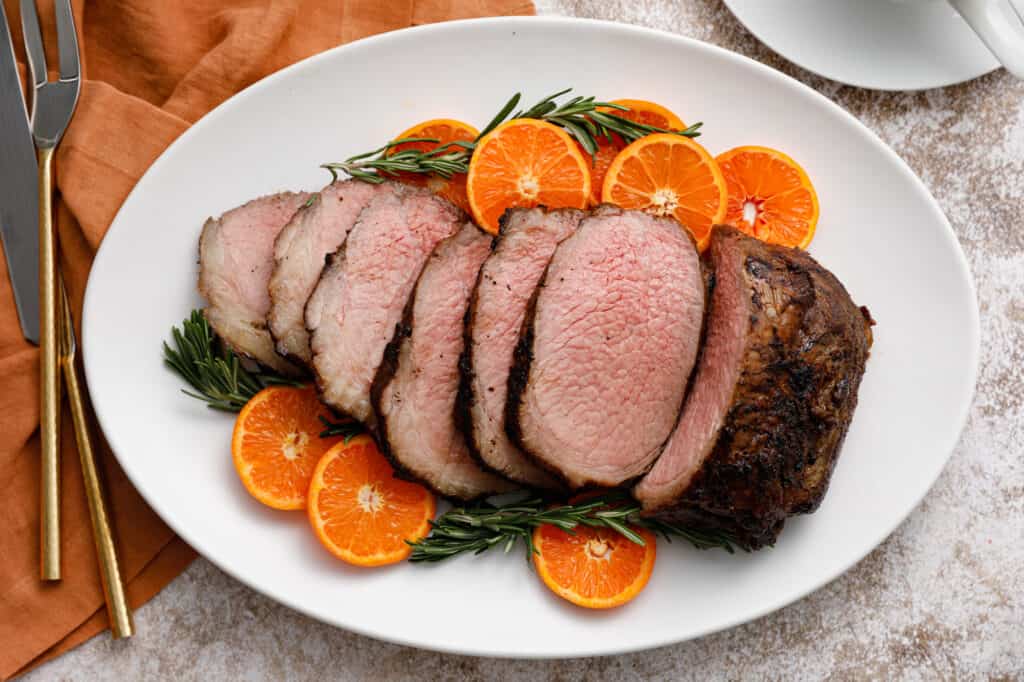 White platter with a sliced beef roast and oranges