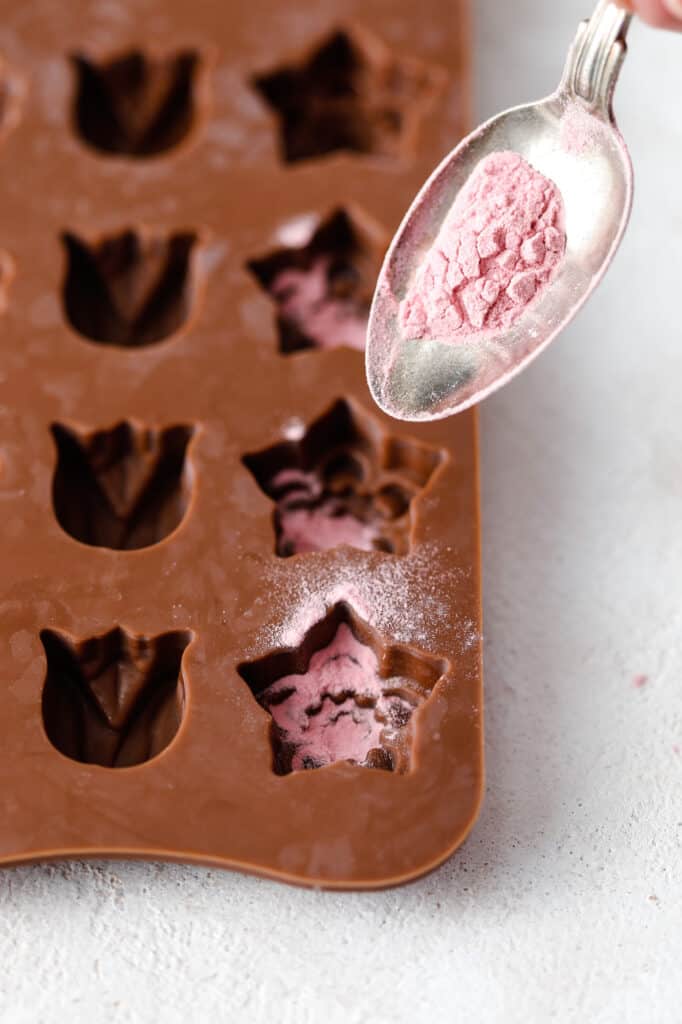 a spoon of pomegranate powder being added to a candy mould