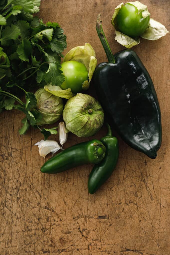 overhead shot on a cutting board with ingredients for salsa including tomatillos, poblano, jalapenos, garlic and cilantro