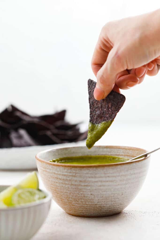 side view of dipping a chip in salsa with chips and limes in the background