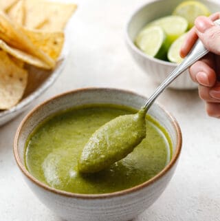 A bowl of bright green jalapeno salsa in a ceramic bowl being scooped with a teaspoon.