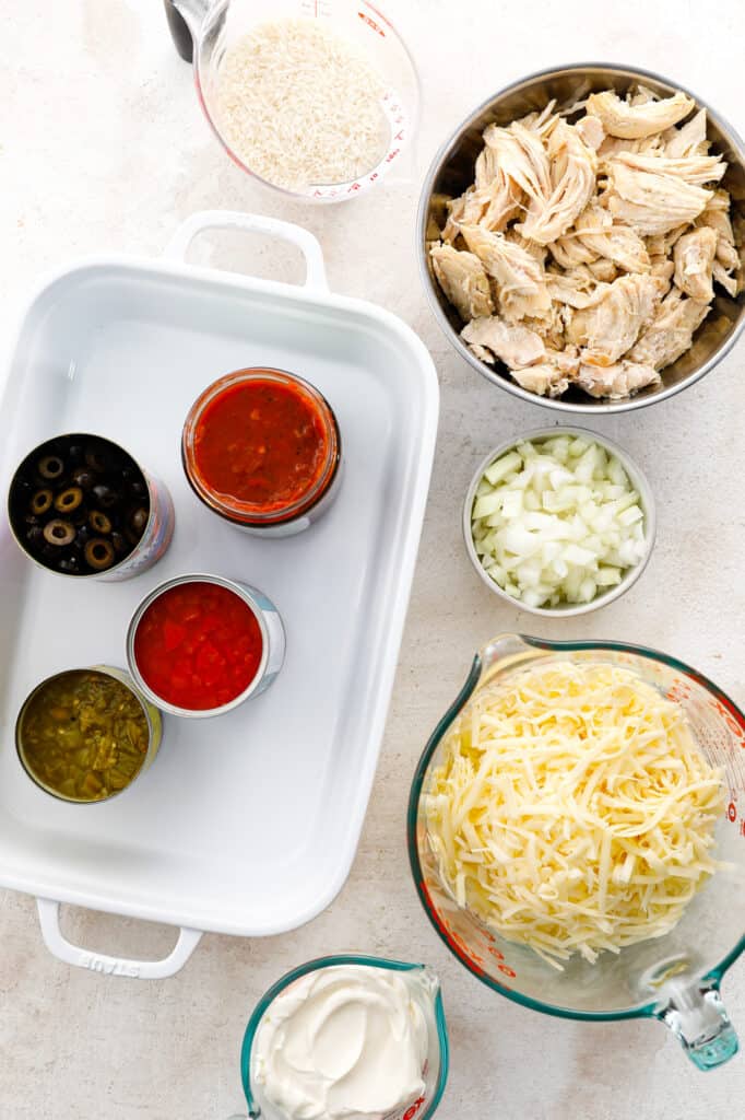 The ingredients for southwest chicken and rice casserole with chicken, onions, cheese, sour cream, tomatoes, salsa, chilies, rice and olives.