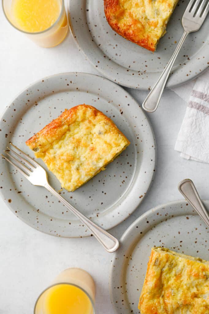 Slice of green chili egg casserole on a grey dish with a fork next to glasses of orange juice