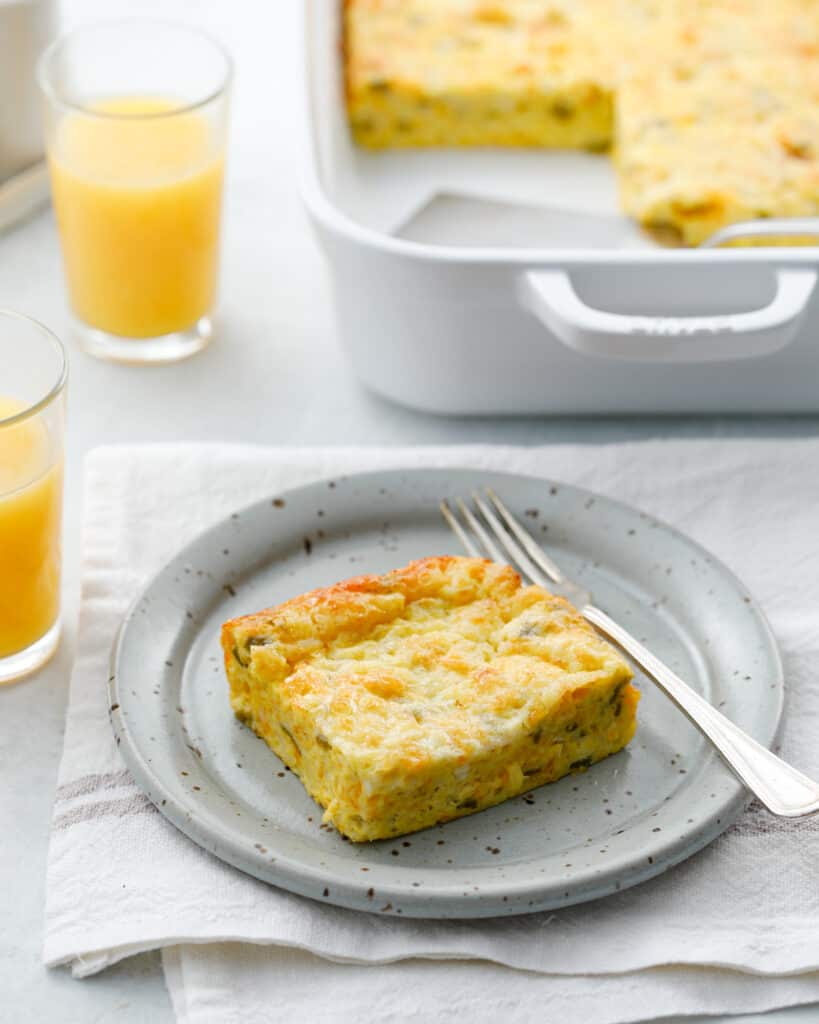 Slice of green chili egg casserole on a grey dish with a fork next to glasses of orange juice