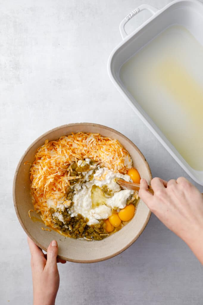 a large bowl mixing together the ingredients: eggs, cottage cheese, chilis, flour, baking powder and shredded cheese