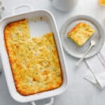 Slice of green chili egg casserole on a grey dish with a fork next to glasses of orange juice and a white napkin in a breakfast scene