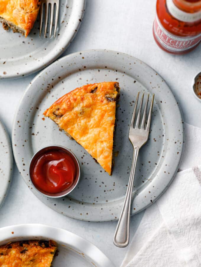 A slice of Impossible Cheeseburger Pie on a plate with a fork and a side of ketchup
