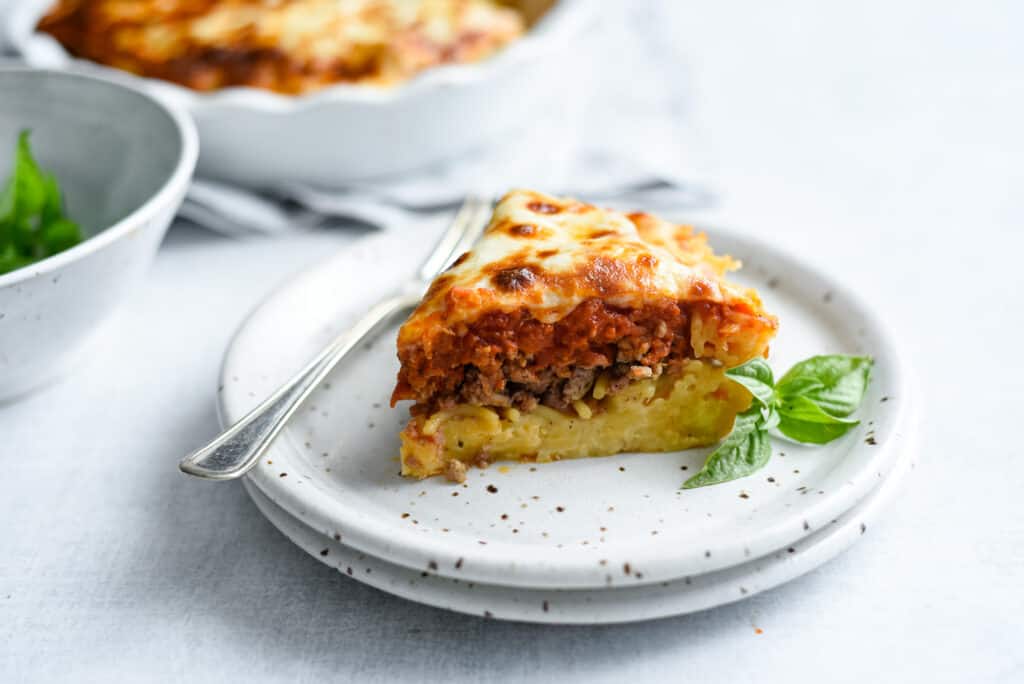 a slice of spaghetti pie on a plate with a fork, a spaghetti crust topped with ground Italian sausage, marinara and mozzarella