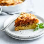 a slice of spaghetti pie on a plate with a fork, a spaghetti crust topped with ground Italian sausage, marinara and mozzarella