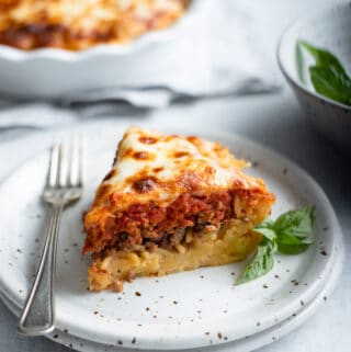 a slice of spaghetti pie on a plate with a fork, a spaghetti crust topped with ground Italian sausage, marinara and mozzarella