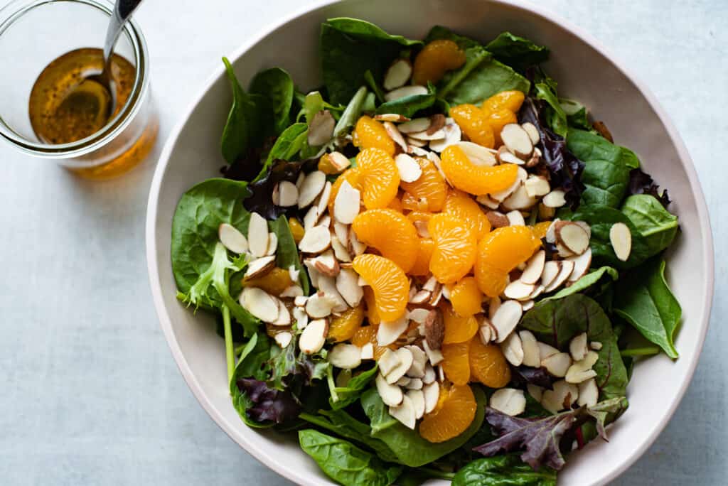 A large bowl filled with mandarin oranges, spinach, almonds and with a side of vinaigrette