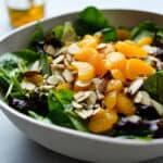 A large bowl filled with mandarin oranges, spinach, almonds and with a side of vinaigrette