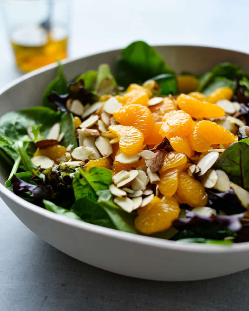 A large bowl filled with mandarin oranges, spinach, almonds and with a side of vinaigrette