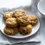 pumpkin chocolate chip cookies on a plate on a blue napkin next to a white mug