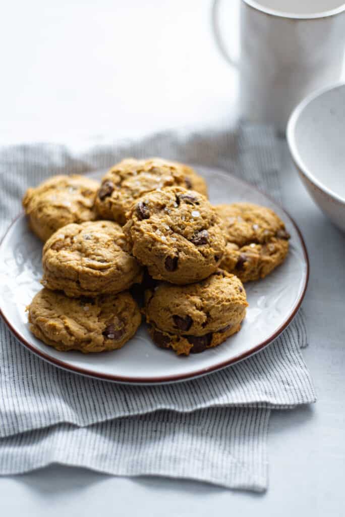 pumpkin chocolate chip cookies on a plate on a blue napkin next to a white mug