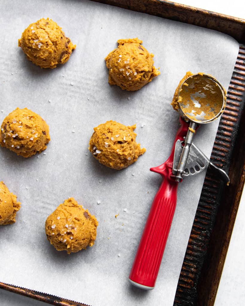 pumpkin chocolate chip cookie dough scooped onto a baking sheet next to a scoop