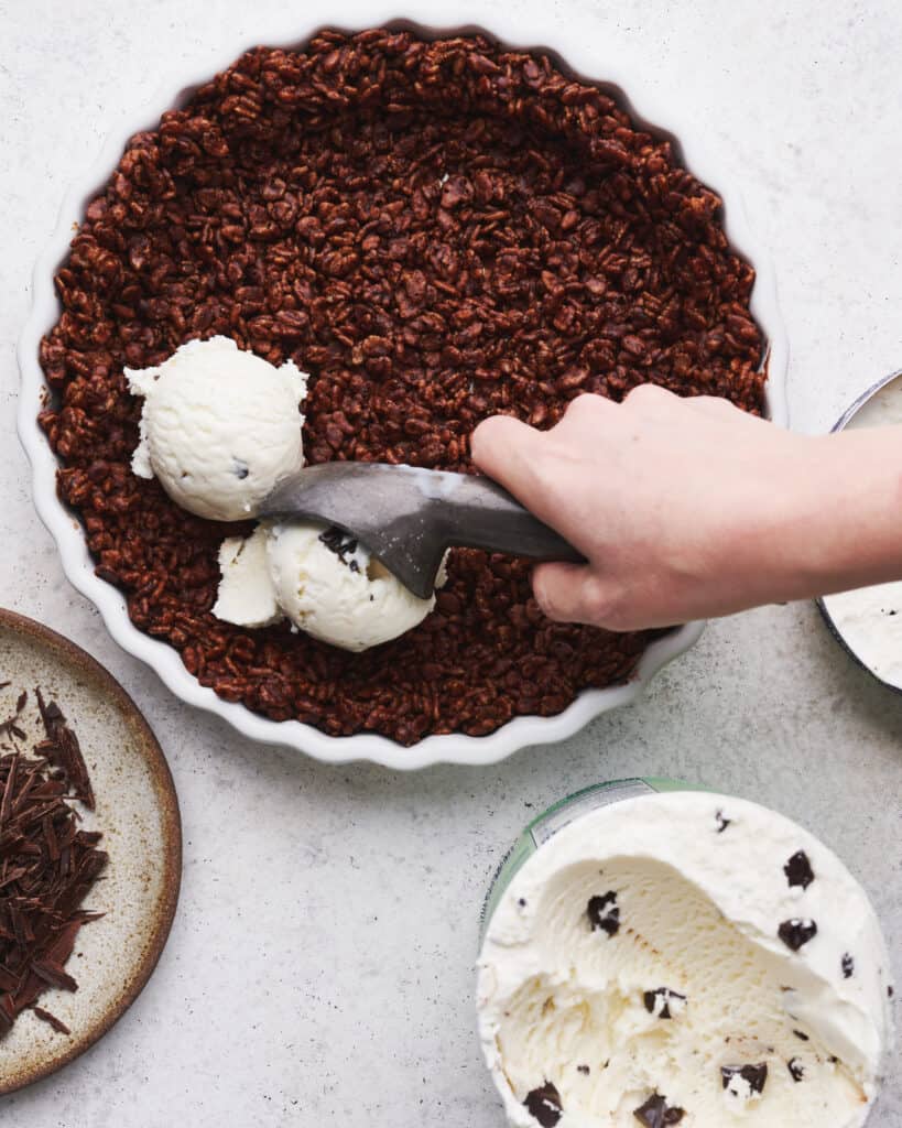 overhead view of scoops of mint chocolate chip ice cream being put into a chocolate Krispie crust