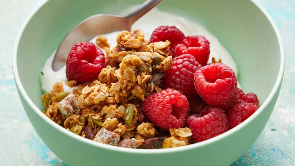 Side view of granola, berries and yogurt in a green bowl