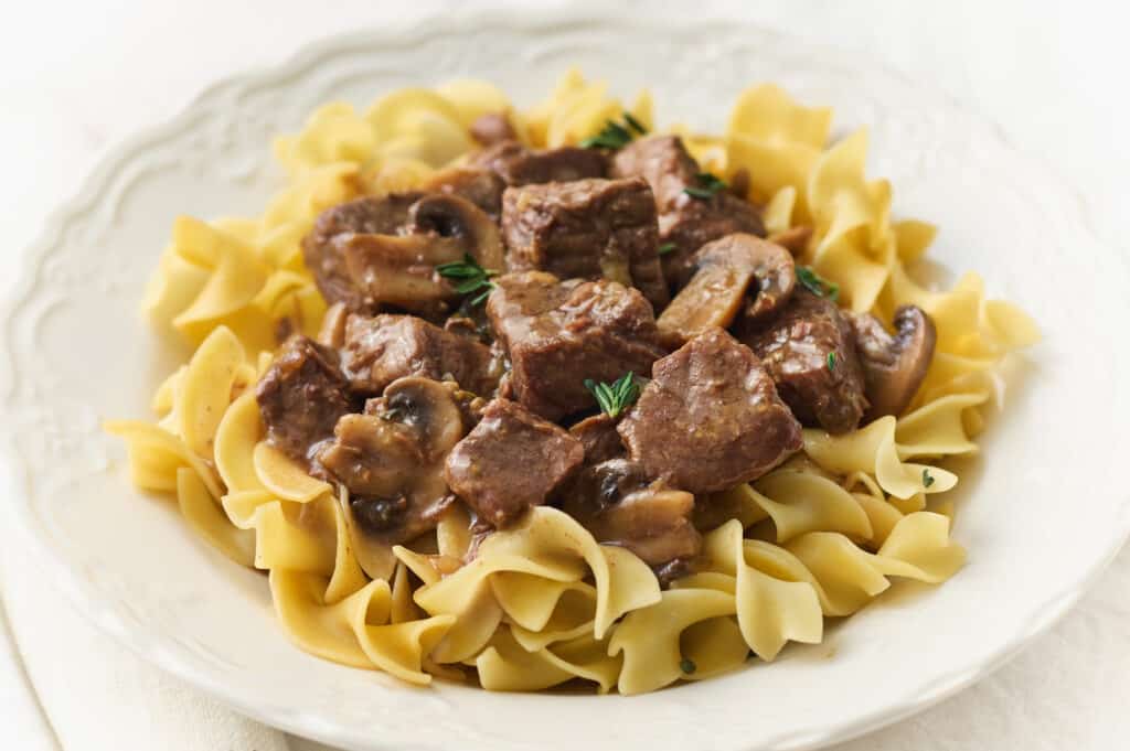 A white dish with beef in gravy over noodles