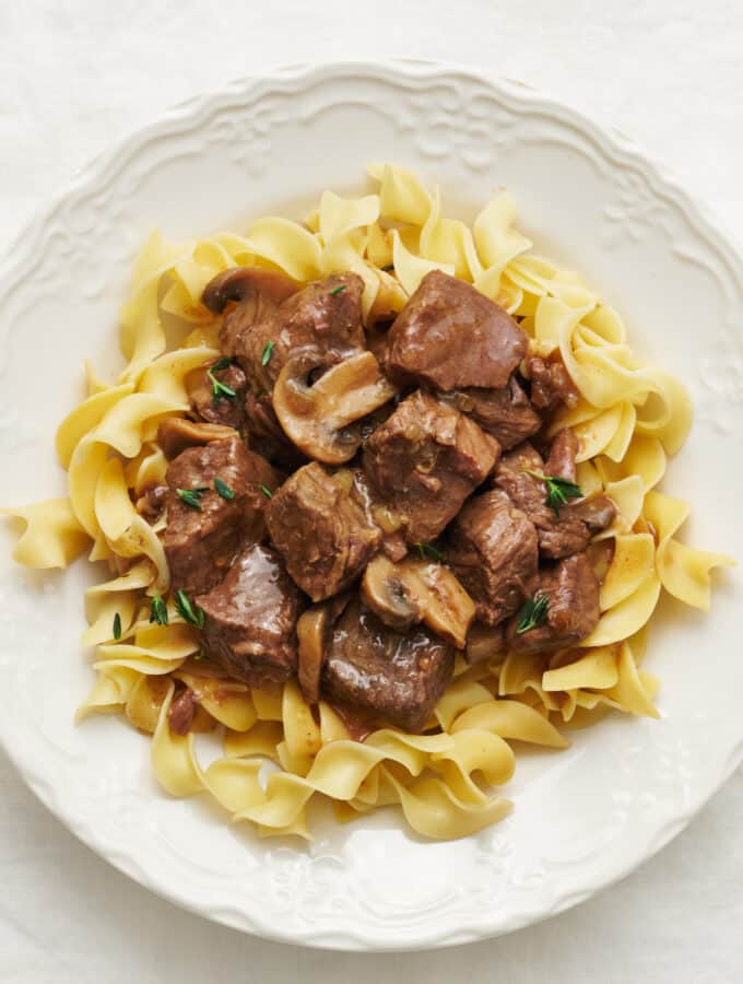Overhead view of a plate of beef tips in gravy with mushrooms over noodles