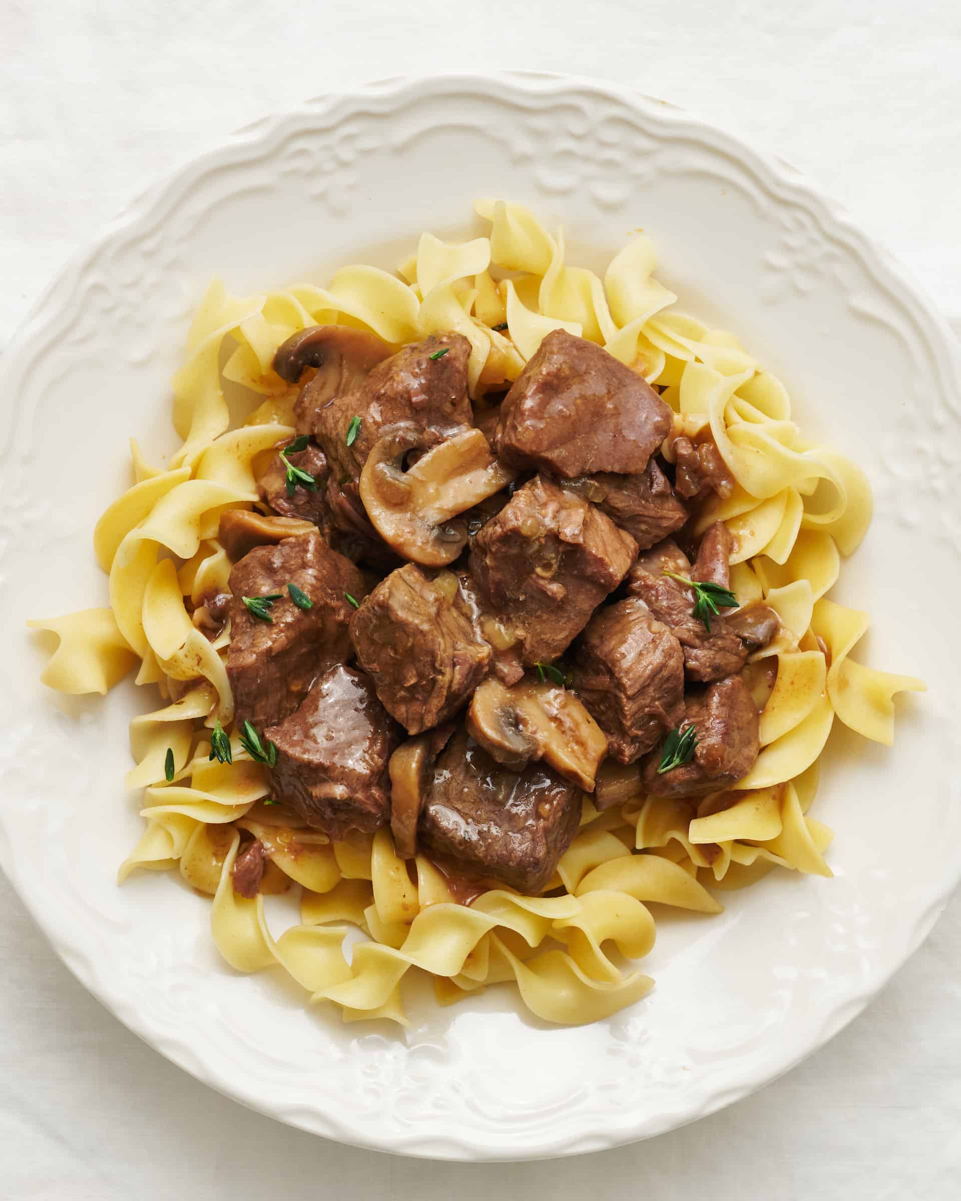 Overhead view of a plate of beef tips in gravy with mushrooms over noodles