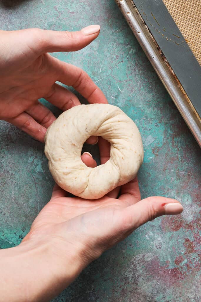 hands showing a fully formed sourdough discard bagel after being shaped