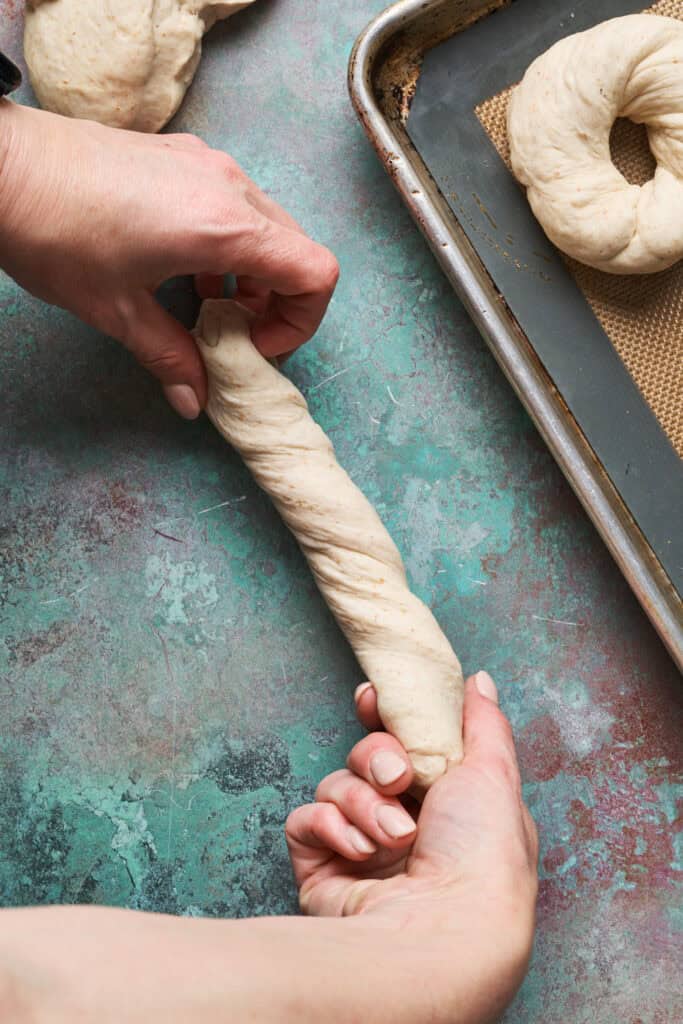 hands showing how to roll the bagel dough into a rope for shaping