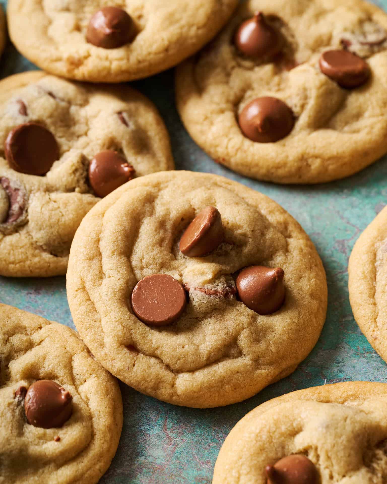 side angle of a chocolate chip cookie with other cookies on a green background