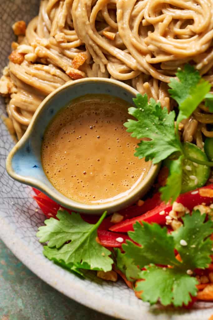 Closeup of a side of peanut sauce in a blue cup nestled into the noodles and cilantro