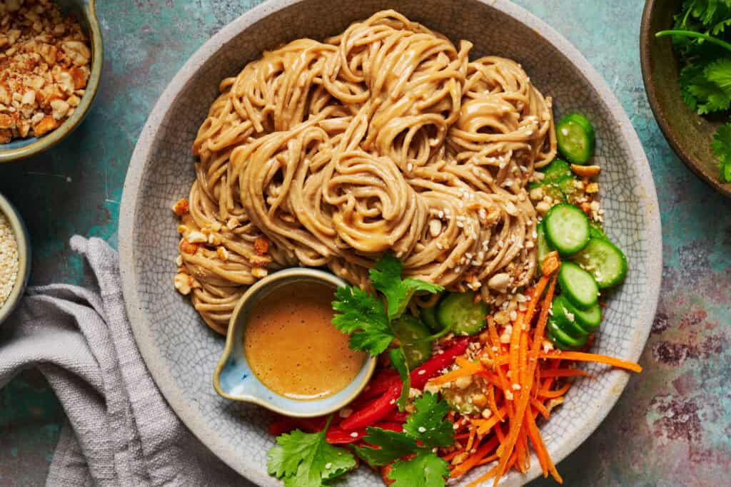 overhead view of a bowl filled with peanut noodles, peanut sauce, and fresh veggies