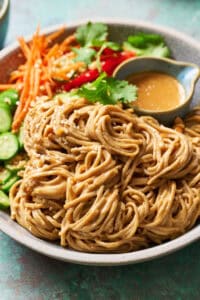 Side view of a bowl of peanut noodles with extra sauce and veggies